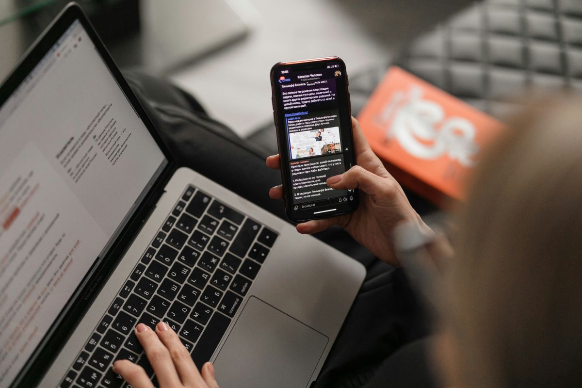 woman using a laptop while reading messages on a smartphone