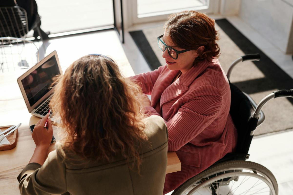 Two women having a discussion at a table, one using a wheelchair 